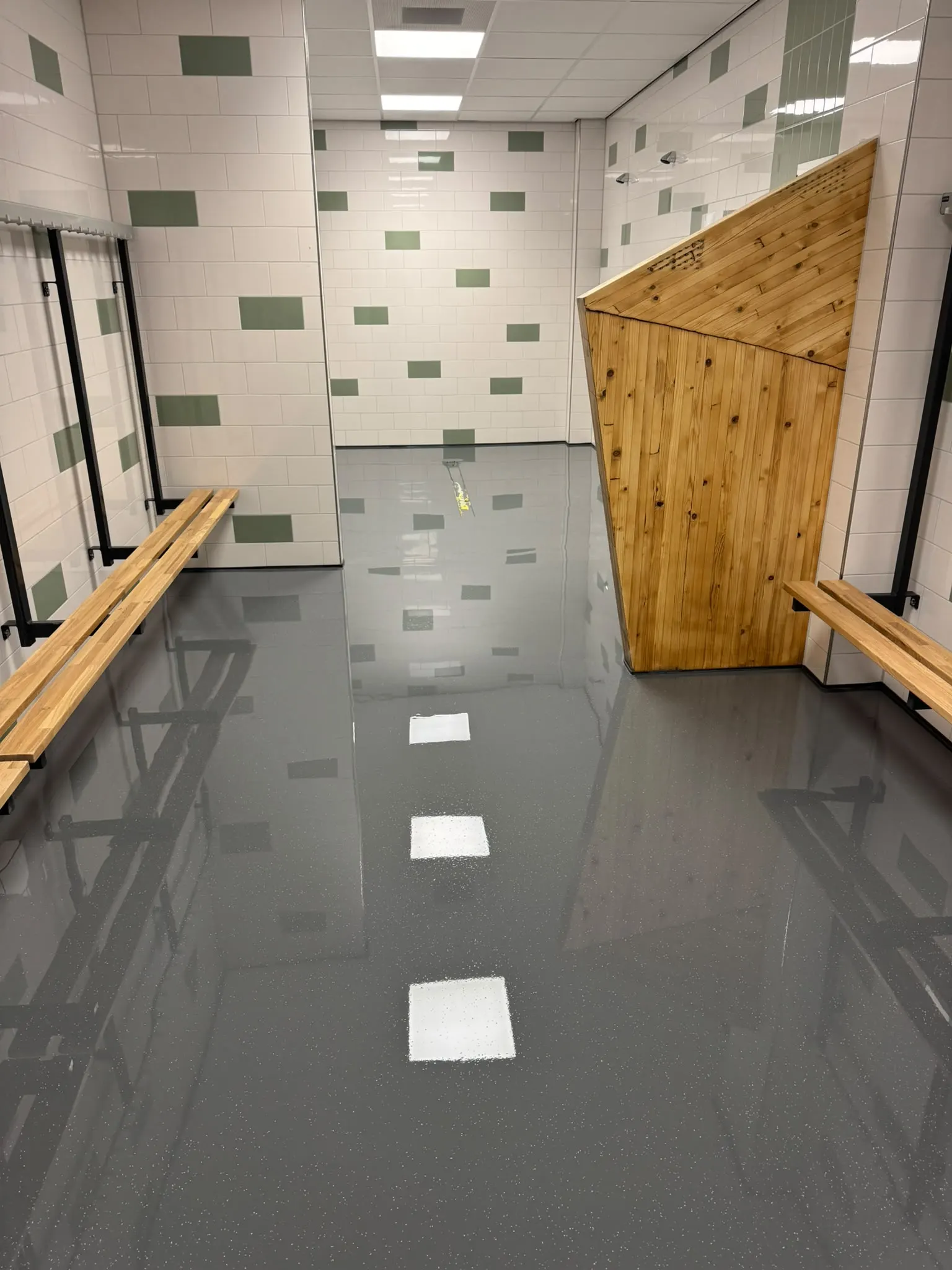 Kleedruimte met houten banken en een glanzende, donkergrijze gietvloer